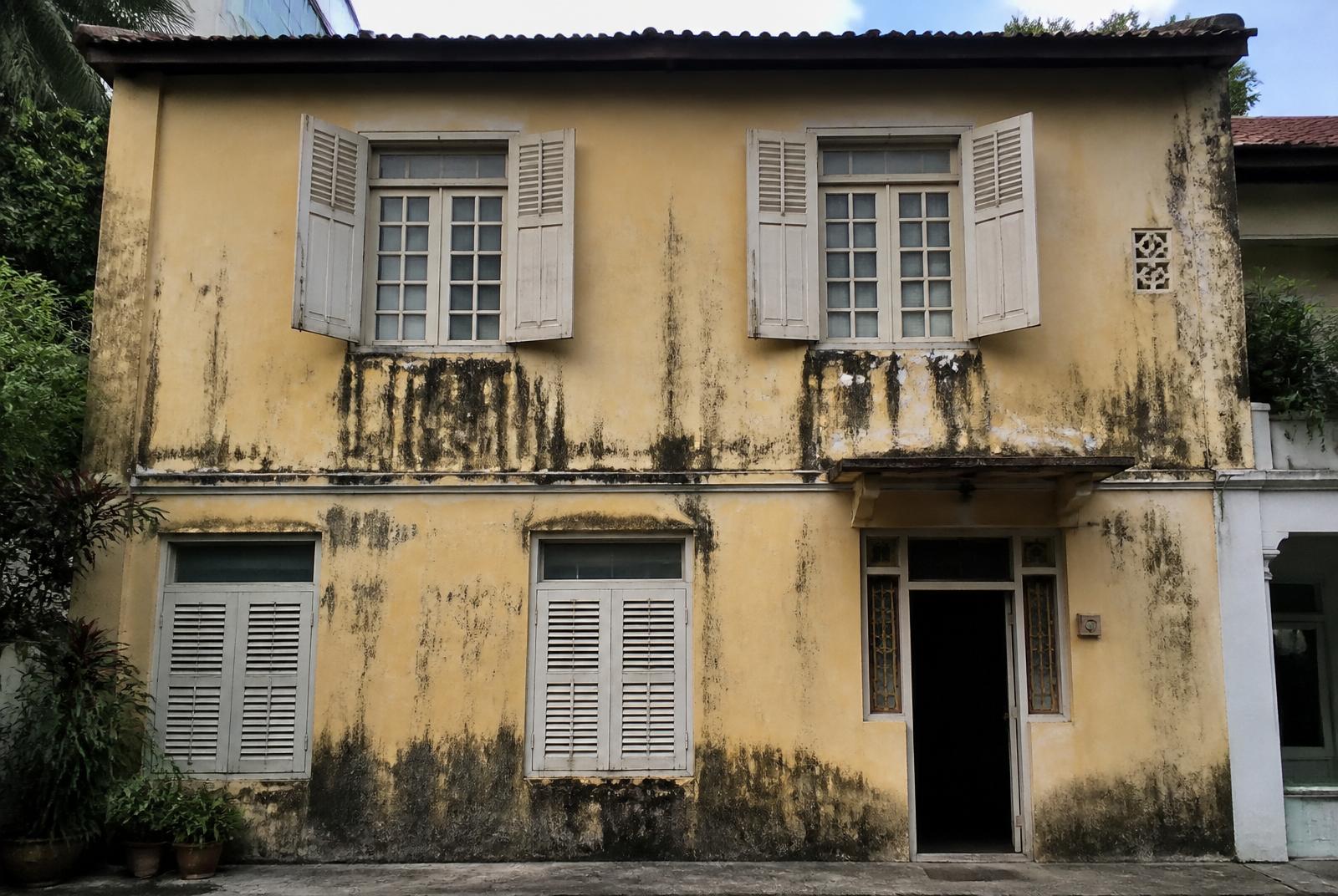 Landed house exterior with mould streaks and faded yellow paint before repaint